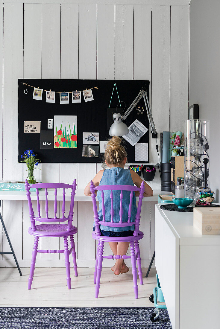 Mädchen auf violettem Stuhl am Schreibtisch mit schwarzer Pinnwand