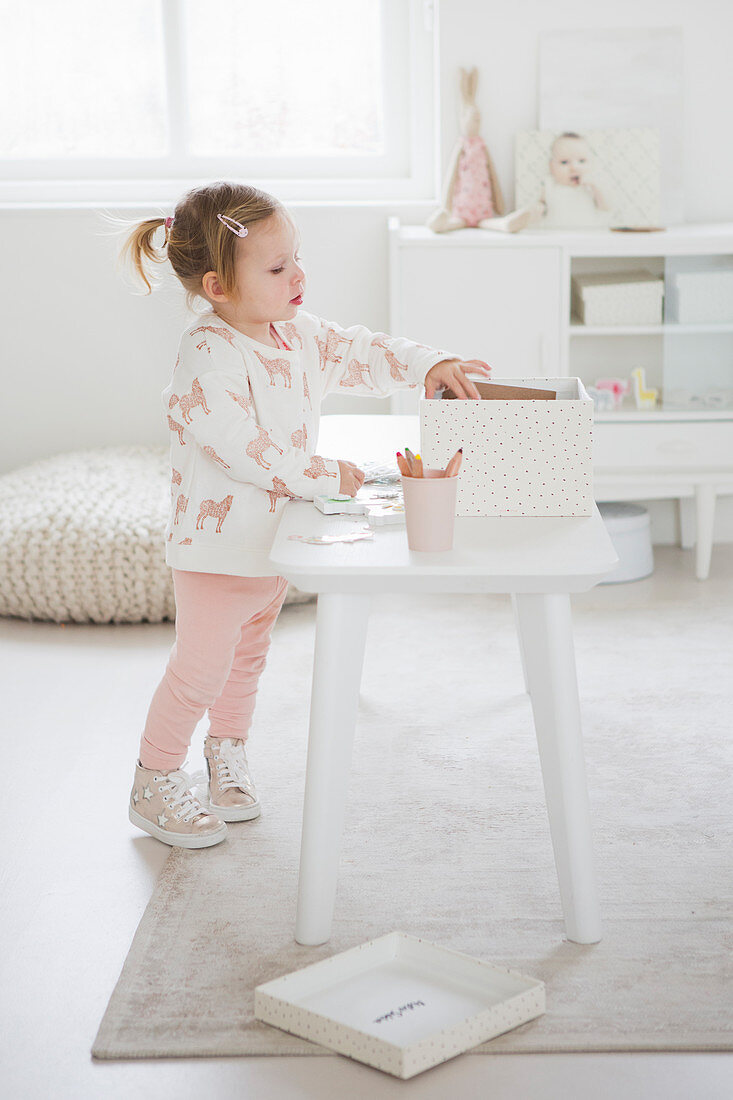 Kleines Mädchen am Spieltisch im Kinderzimmer ganz in Weiß