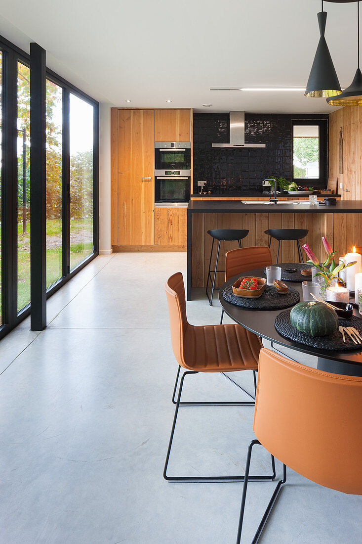 Round dining table and brown chairs in front of open-plan kitchen with glass wall
