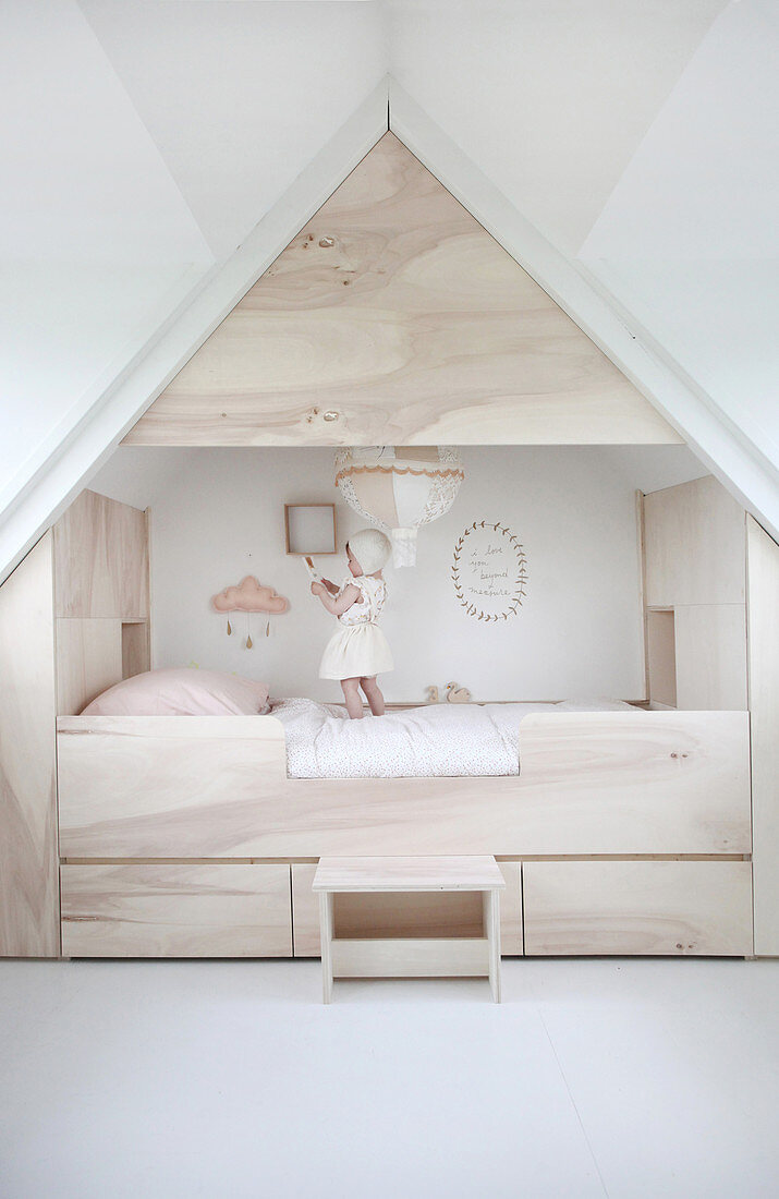Child standing on modern cubby bed surrounded by storage in attic bedroom