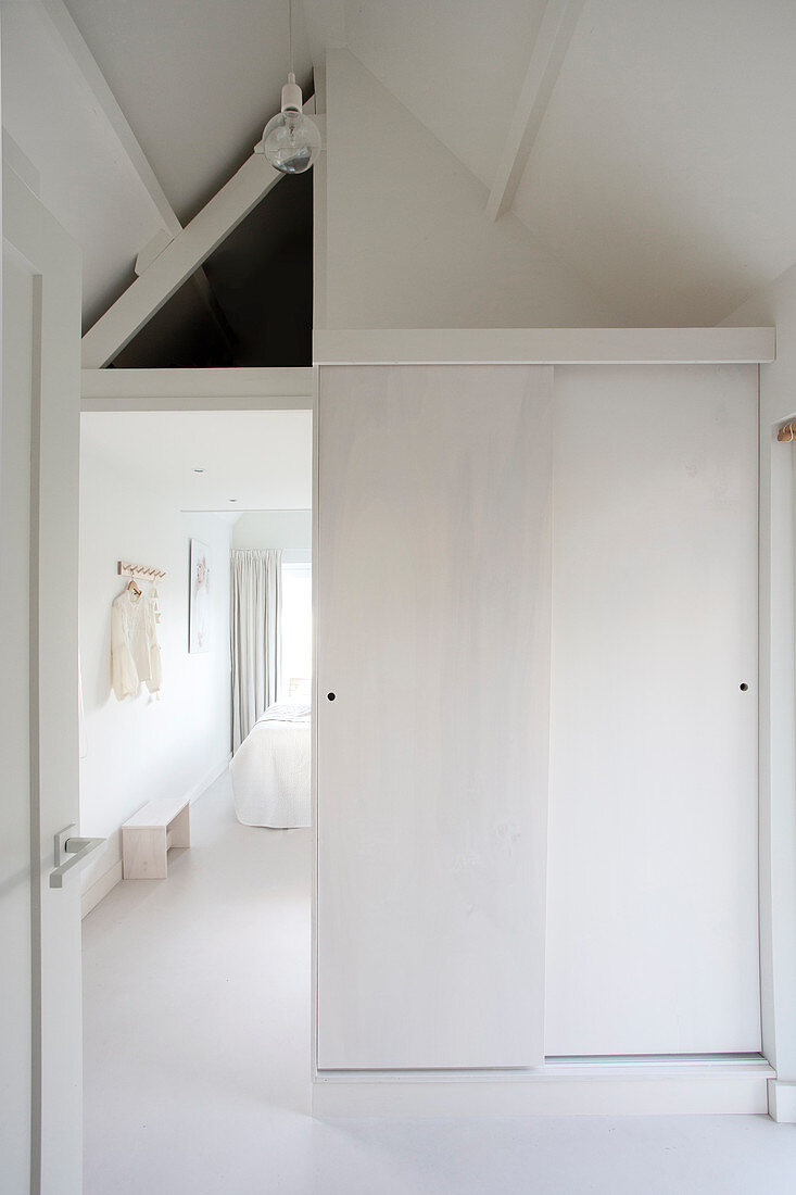 Sliding door leading into white attic bedroom