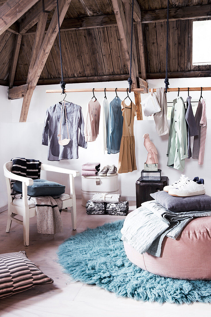 Clothes rail below wooden ceiling in rustic bedroom in pastel shades