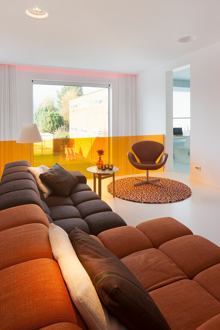 Wohnzimmer mit orangefarbenem Raumteiler, Designer-Sessel und Designer-Sofa