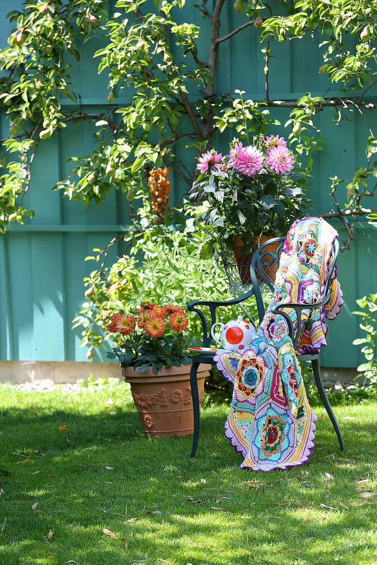 Multi-coloured crocheted blanket on chair on lawn in garden