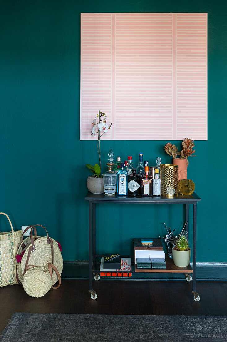 Bar trolley with spirits in front of dark green wall with pink artwork