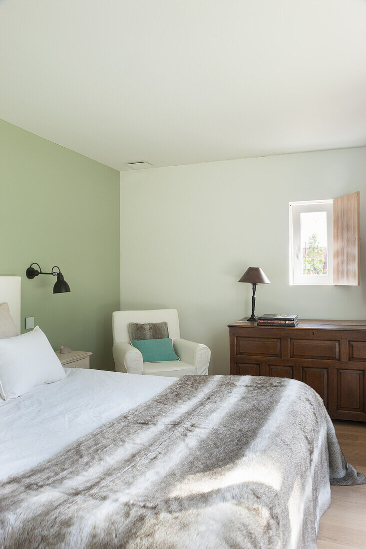 Schlafzimmer mit grüner Wand, Holzmöbeln und Wolldecke auf dem Bett