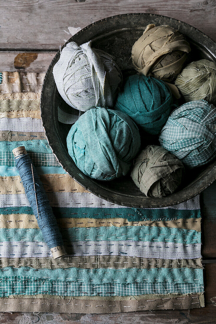 Strips of fabric in shades of blue and green with spools of thread and bowl full of balls of fabric