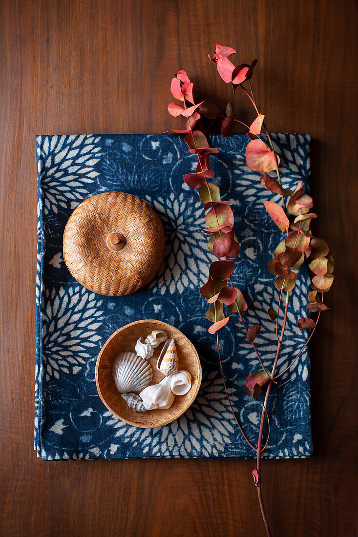 Eucalyptus sprig in Autumn colours and seashells in basket on blue fabric