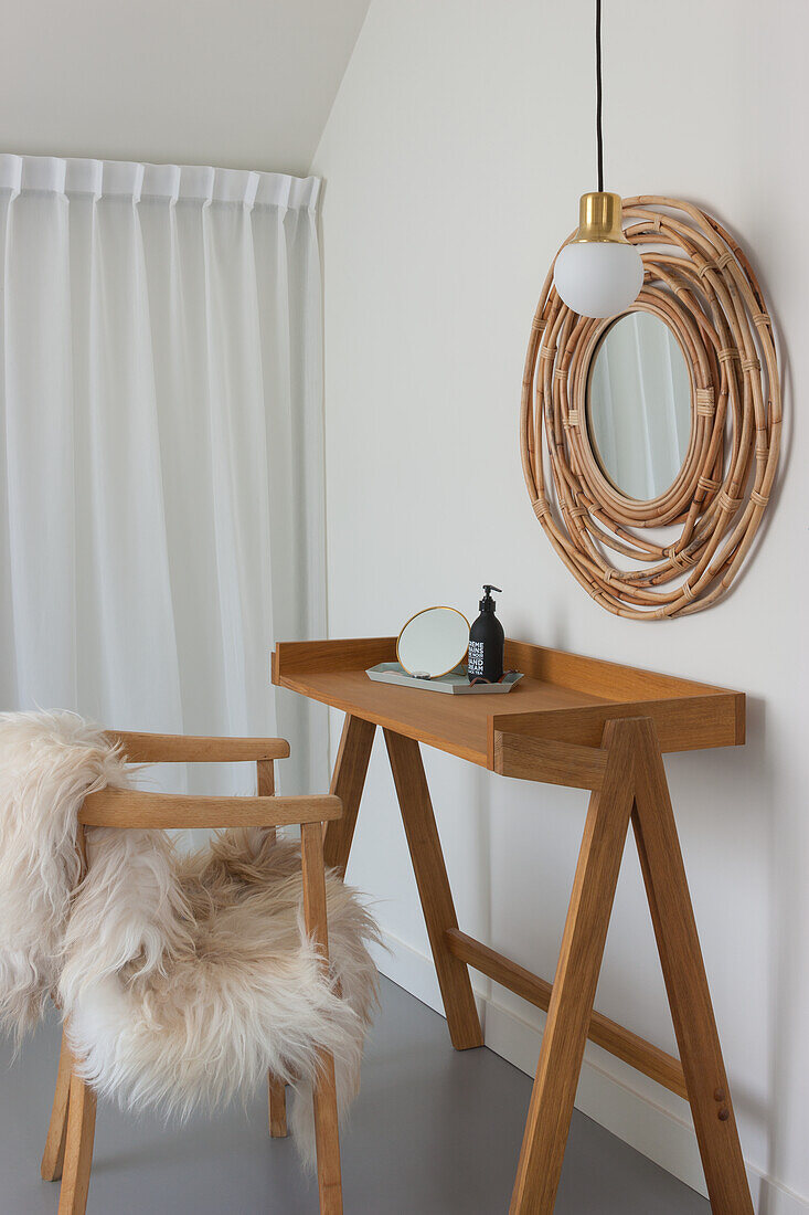 Holzkonsole und Stuhl mit Felldecke, runder Bambus-Spiegel an weißer Wand