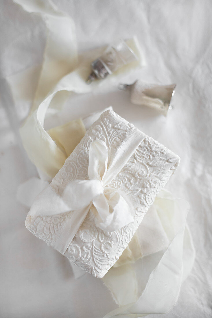 In weißen Stoff mit Ornamenten verpacktes Geschenk mit Stoffband