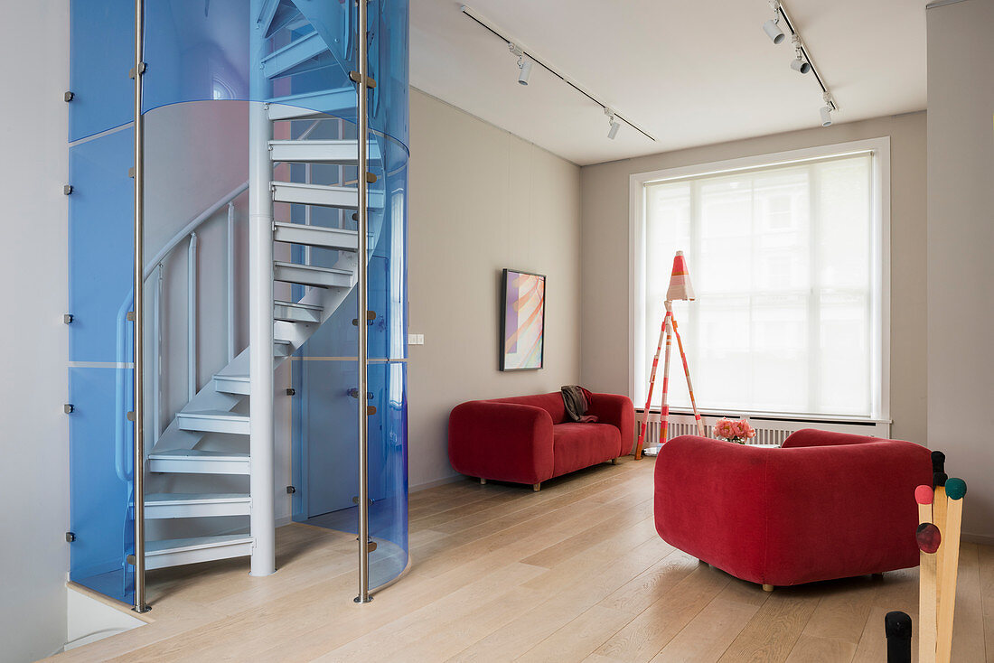 Wendeltreppe mit blauer Glaswand im Wohnzimmer mit rotem Sofa