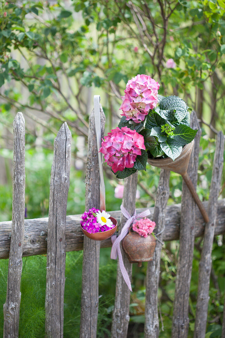 Rusty kitchen utensils decorating garden fence and hydrangeas in old funnel