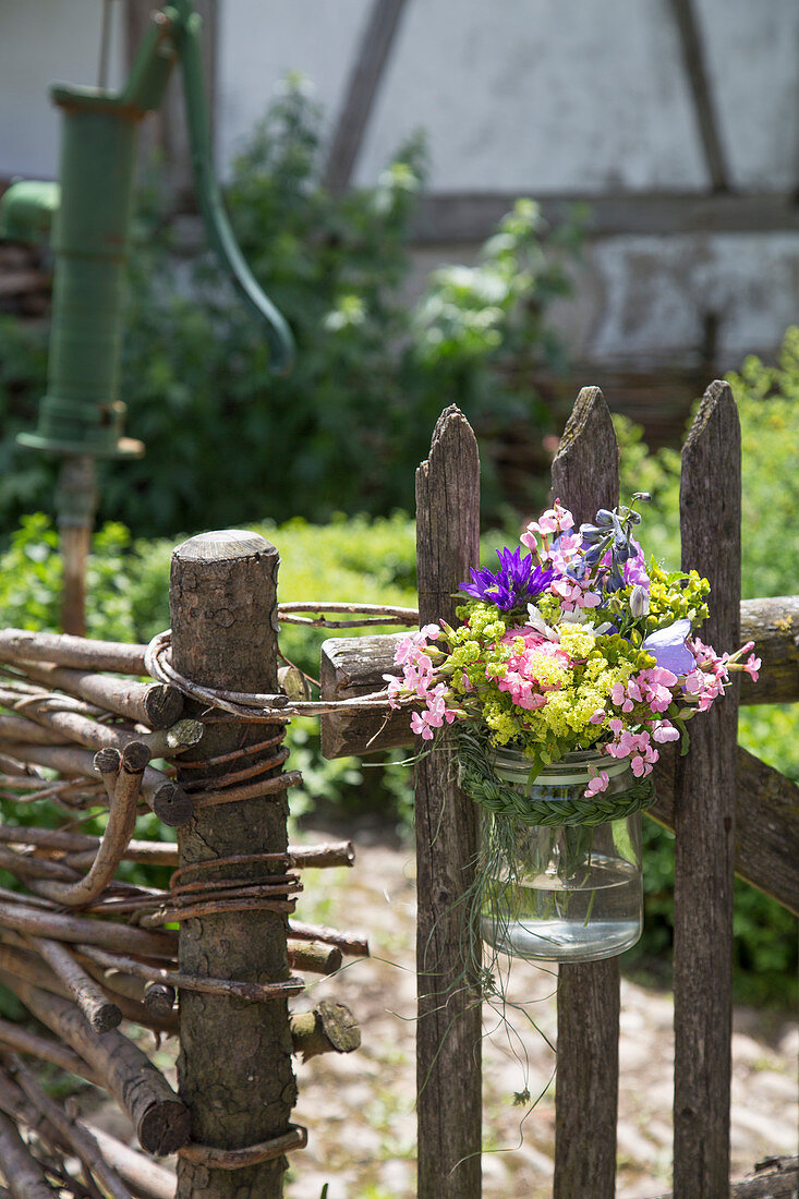 Summer bouquet in preserving jar tied to garden fence