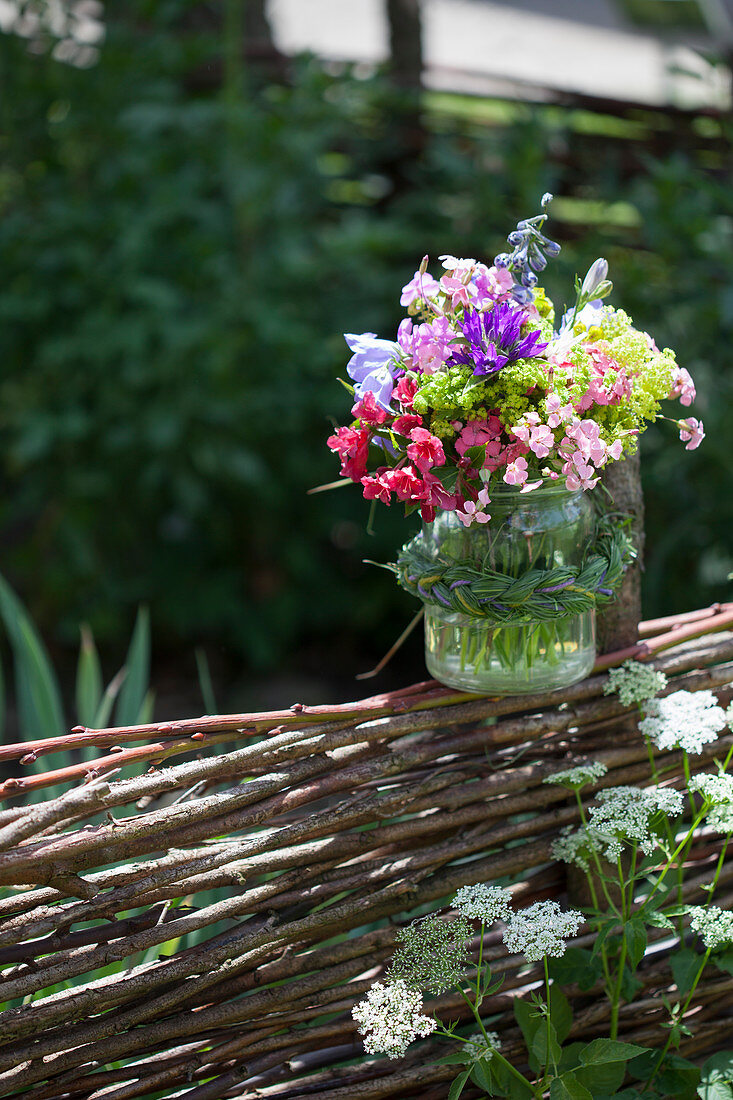 Bouquet in preserving jar with grass braid on top of wattle fence