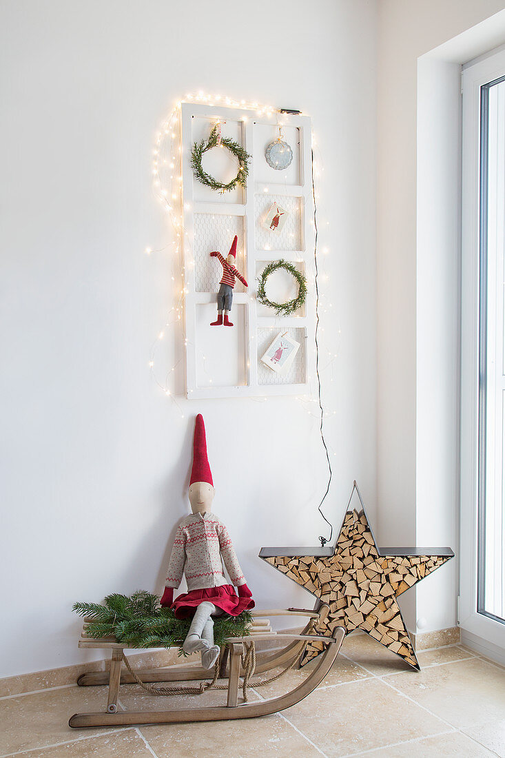 Weihnachtlich dekorierter Rahmen überm Holzschlitten mit Stoffzwerg