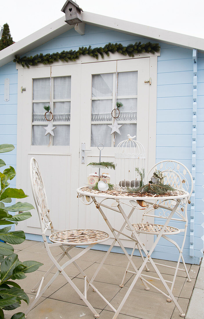 Nostalgische Gartenmöbel aus Metall vorm hellblauen Gartenhaus