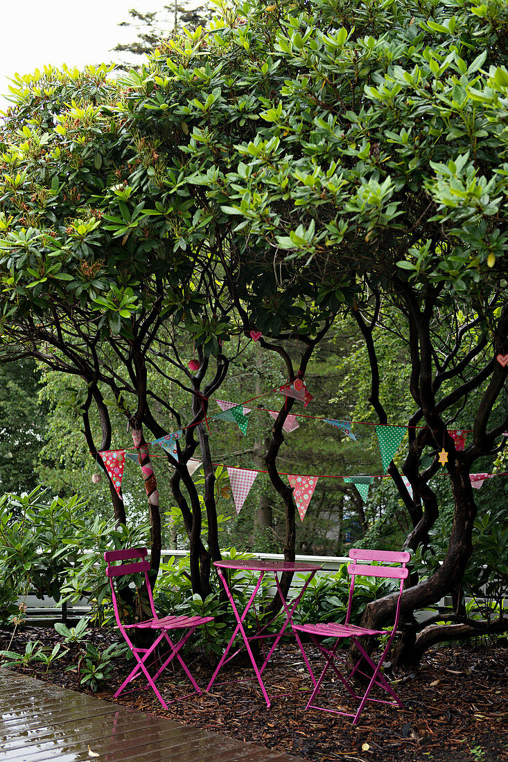 Pinke Gartenmöbel unterm Baum mit Wimpelketten im Garten