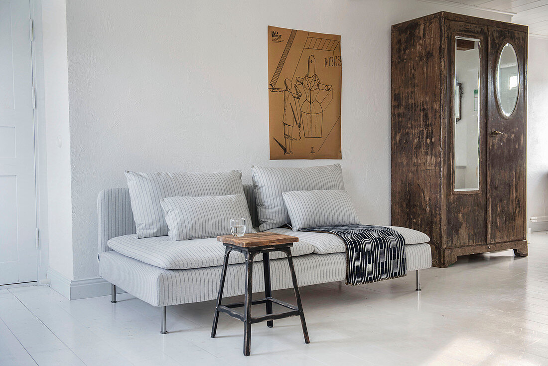 Hocker als Couchtisch vorm grau gestreiften Sofa auf weißem Boden