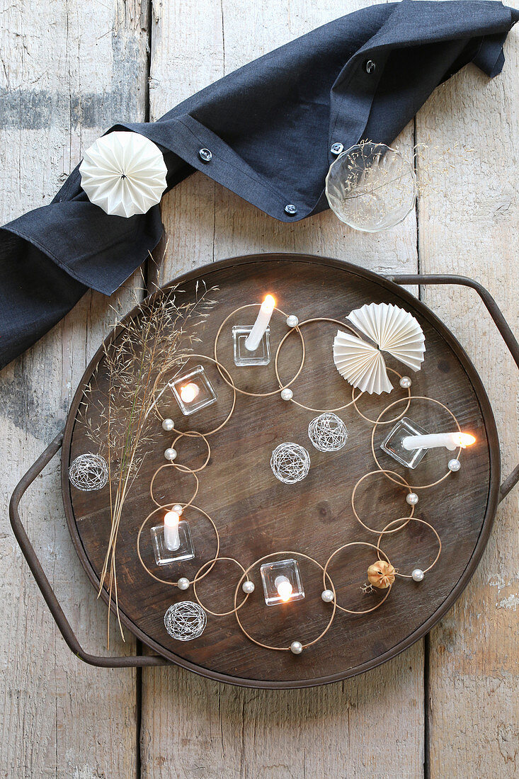 Origineller Tischschmuck aus Glas, Drahtbällen, Perlen und Ringen mit Kerzen auf Holztablett