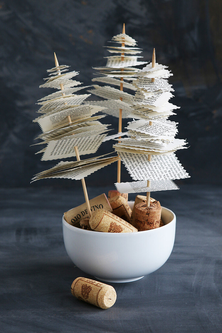Miniature fir trees made from skewered book pages on cork bases against black background