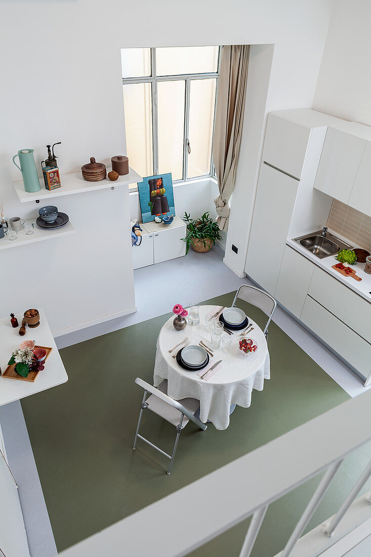 Blick von Galerieebene auf Wohnraum in Weiß mit Küchenzeile und Esstisch