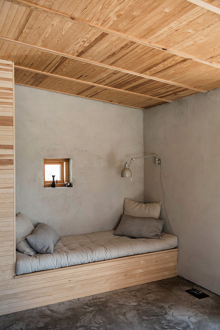 Sitzecke mit Bank in einer Nische mit grauer Wand und Holzdecke