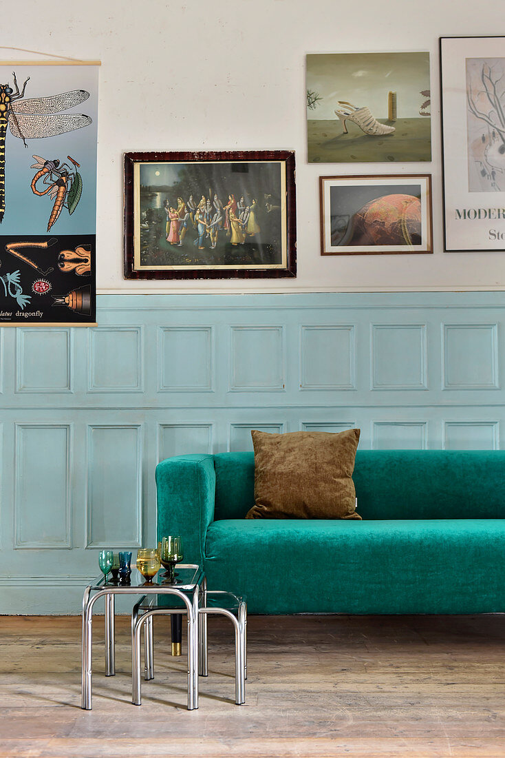 Smaragdgrünes Sofa vor hellblauer Kassettenwand und Bildergalerie