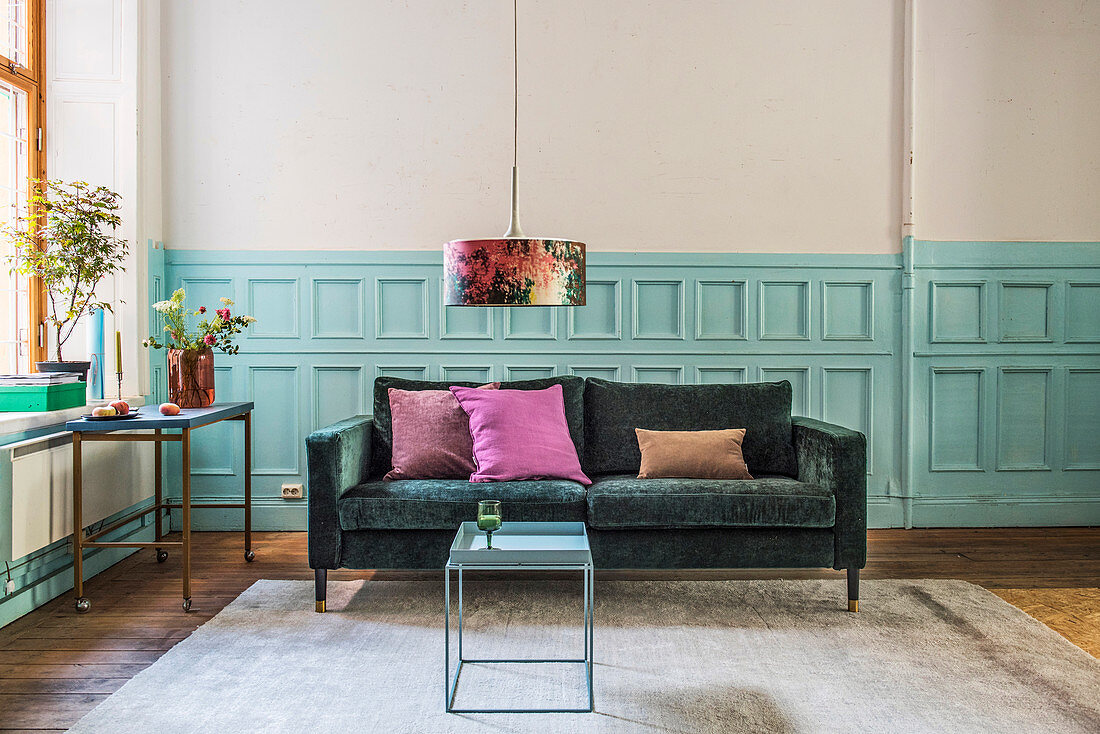 Smaragdgrünes Sofa vor hellblauer Kassettenwand im Wohnzimmer