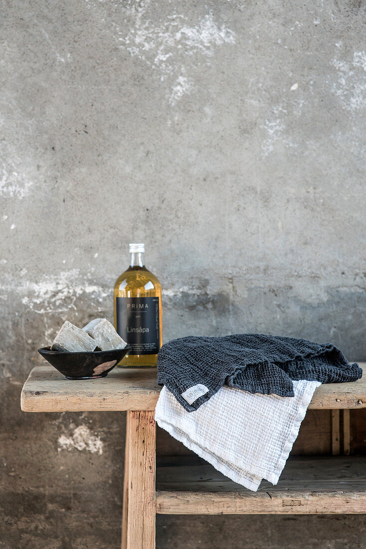 Towels, bottle and bowl of soaps on wooden bench
