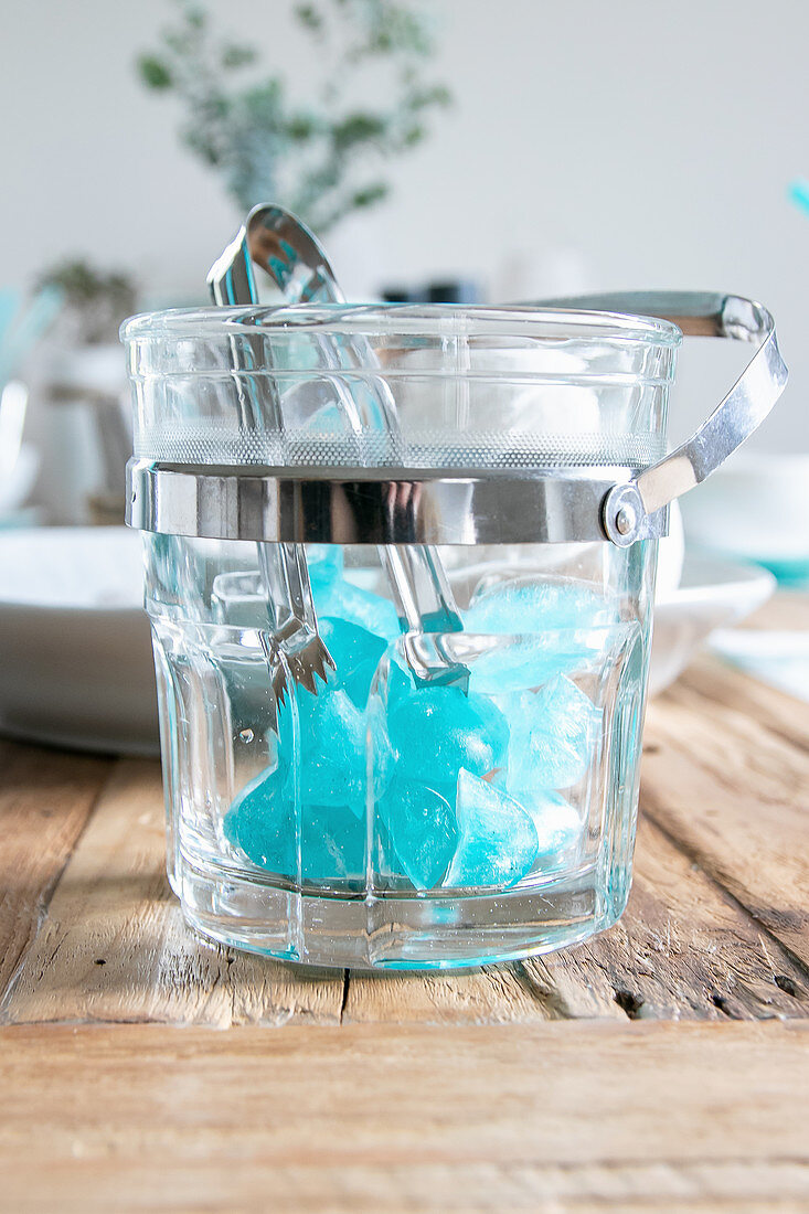 Blue ice cubes and tongs in transparent ice bucket