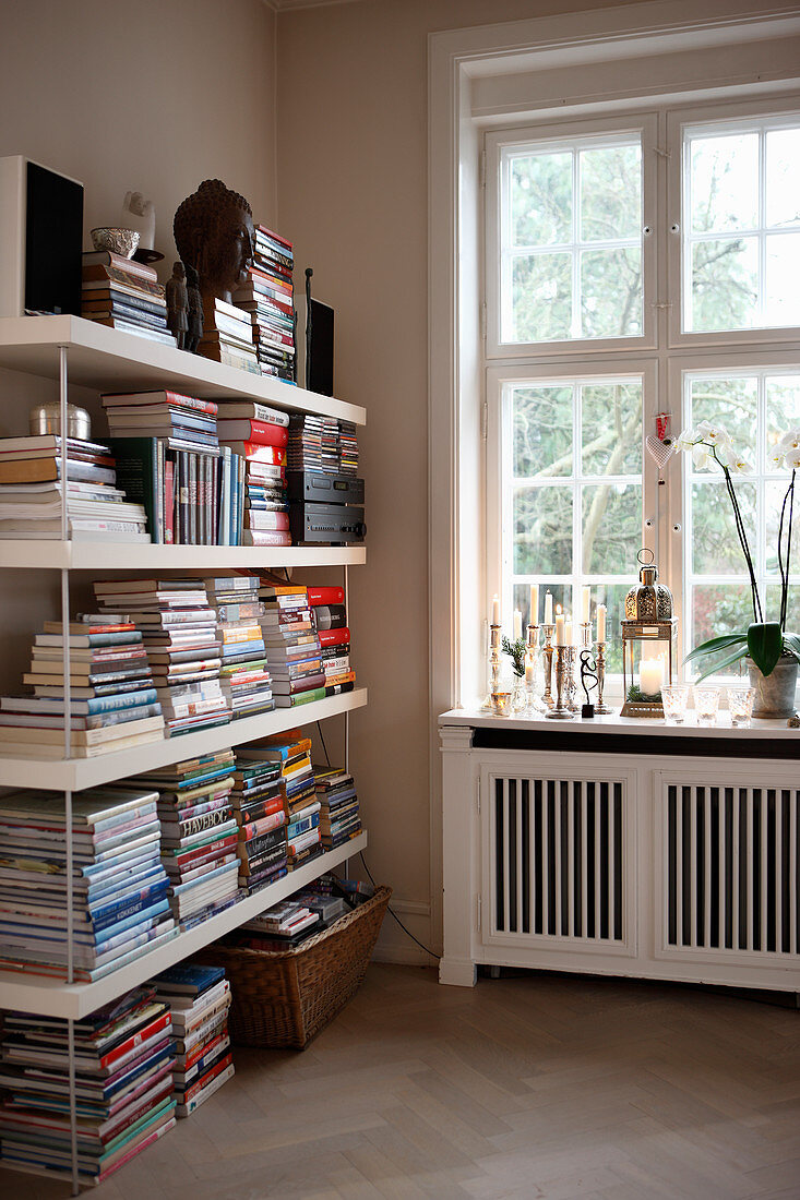 Regal mit gestapelten Büchern am Fenster mit Heizungsverkleidung