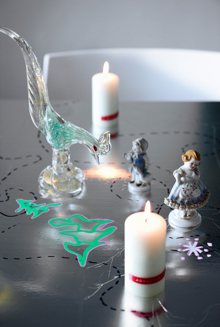 Kerzen, Porzellan- und Glasfiguren auf weihnachtlich bemaltem Tisch