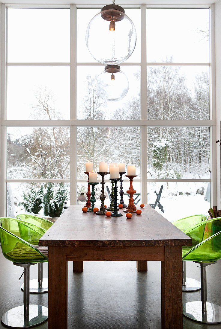 Green acrylic chairs around wooden table next to window with view of snowy garden