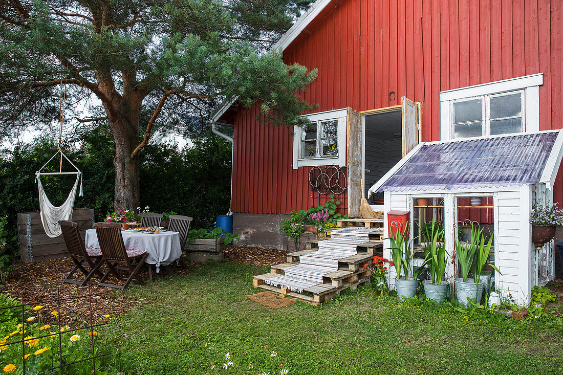 Sommerlicher Garten und Gewächshaus am roten Holzhaus