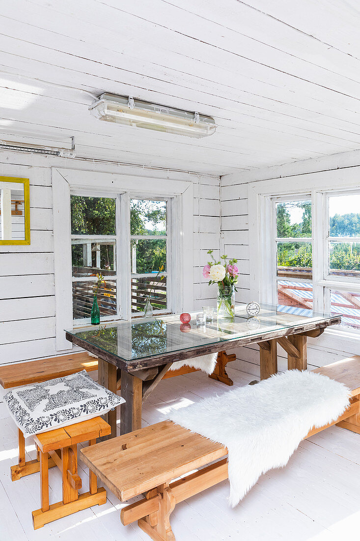 Benches around table with glass top in summery wooden house