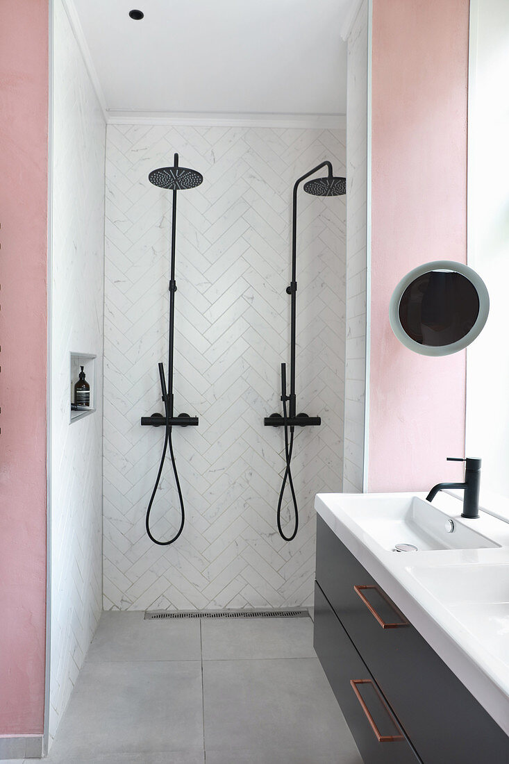 Two shower heads in walk-in shower in pink, modern bathroom
