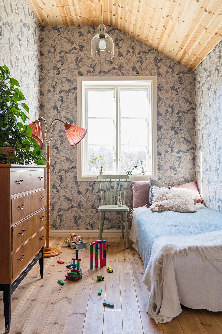 Blue, vintage-style wallpaper and wooden floor in small, child's bedroom