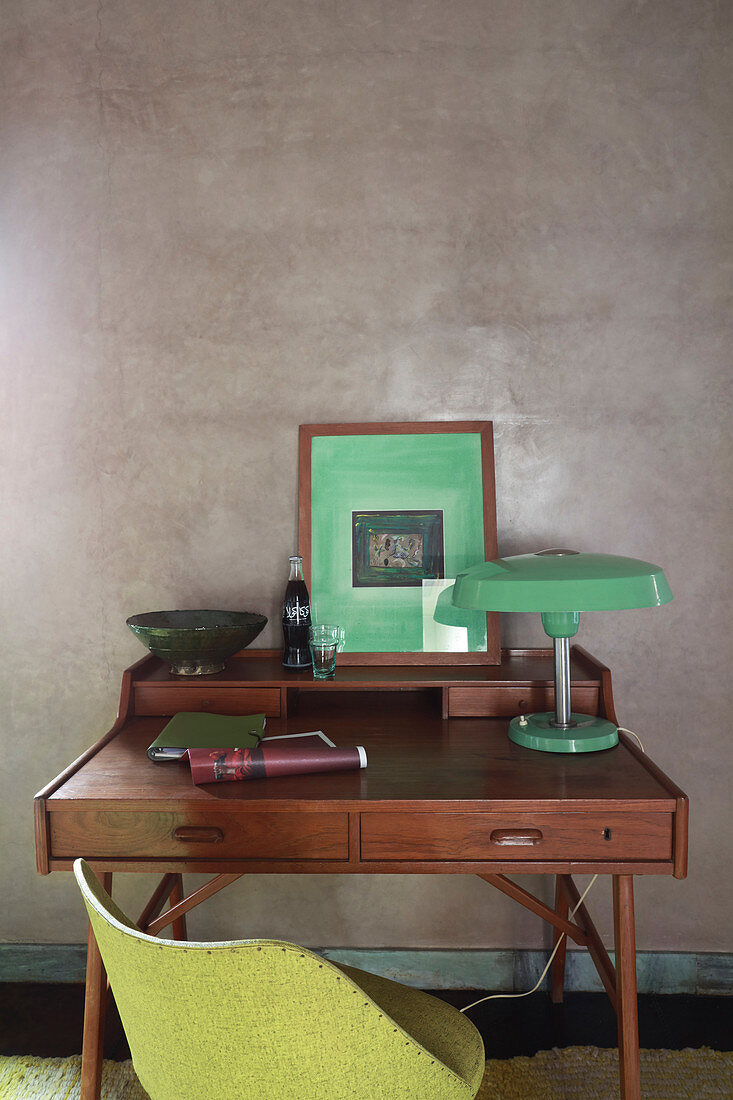 Grüne Tischleuchte und Bild auf dem Schreibtisch vor grauer Wand