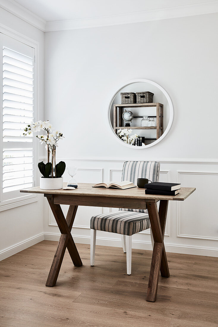 Bücher und Orchidee auf Holztisch, Stuhl mit gestreiftem Bezug und runder Spiegel an der Wand