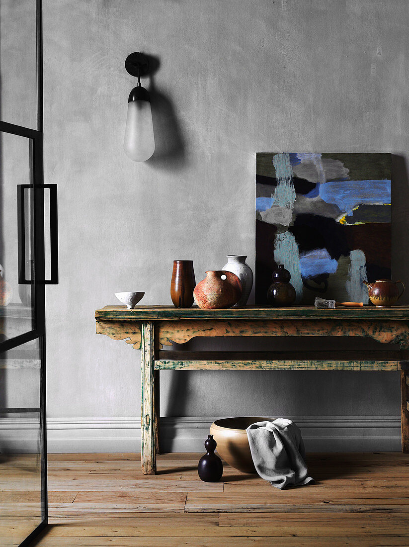 Rustikaler Holztisch mit Keramik und Malerei vor grauer Wand