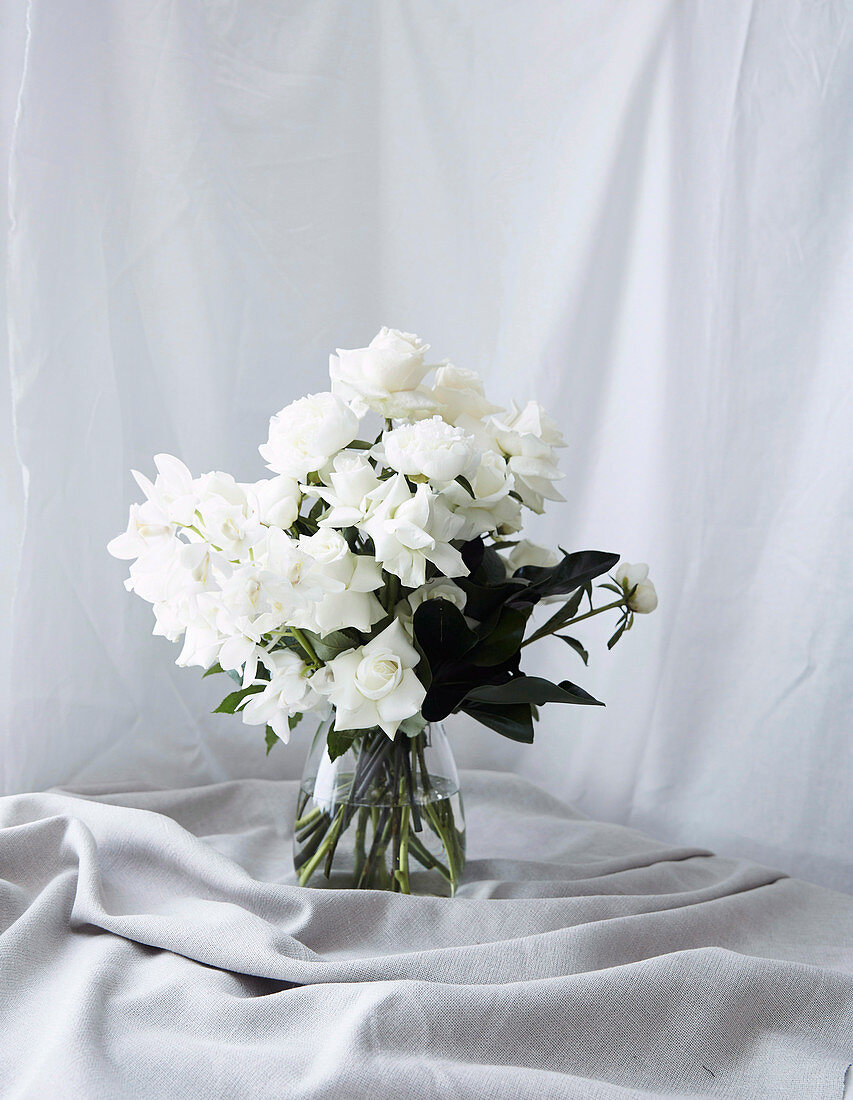 Weiße Rosen und grüne Blätter in Glasvase