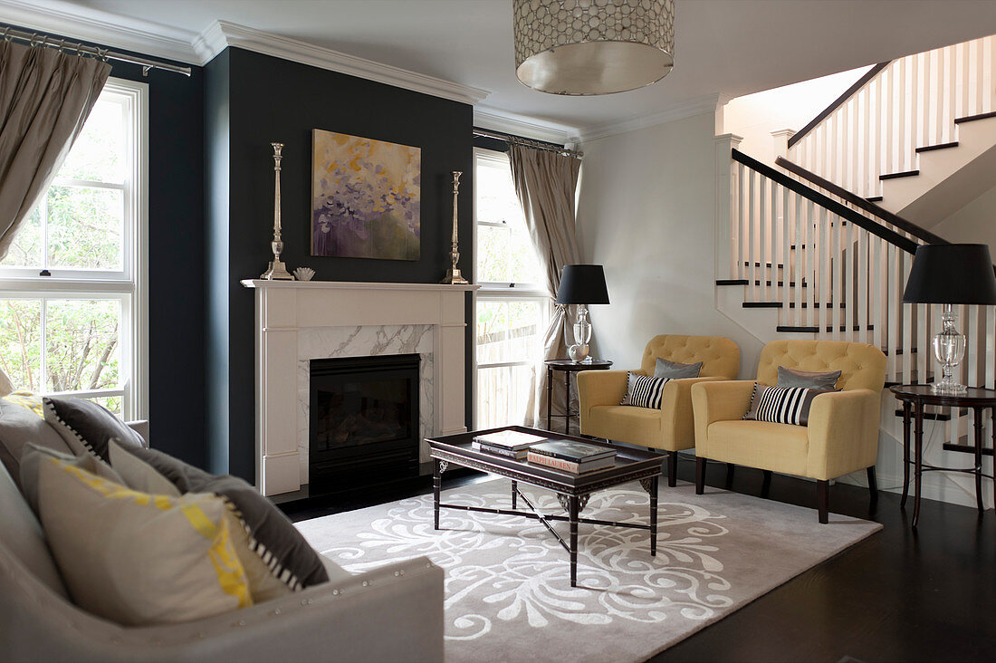 Pastellfarbene Polstersessel und Couchtisch im Wohnzimmer mit schwarz gestrichener Kaminwand, im Hintergrund Treppe