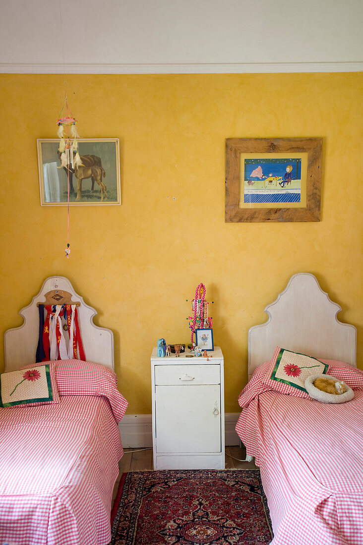 Zwei Einzelbetten aus Holz mit rot-weiß karierter Bettwäsche und Nachtschränkchen im Geschwisterzimmer mit sonnengelber Wand