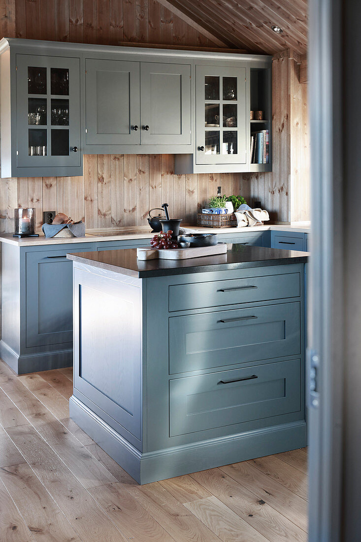 Blue-grey kitchen with island counter in cottage with wooden walls and gable roof