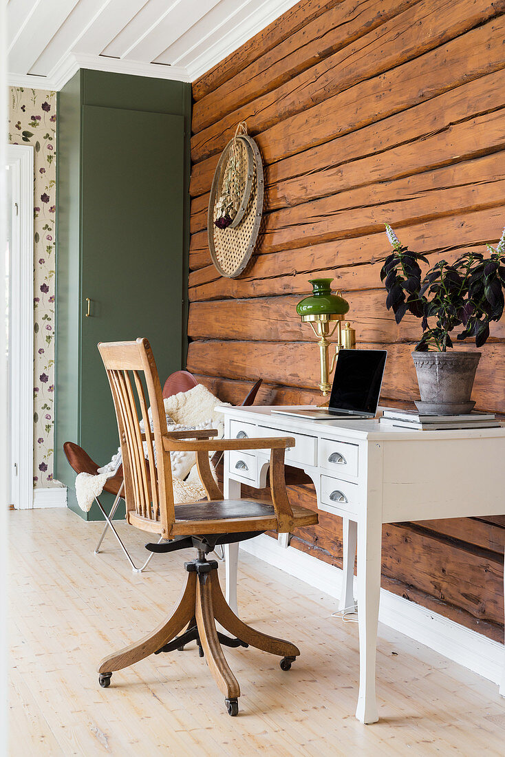 Desk and old swivel chair against rustic log-cabin wall