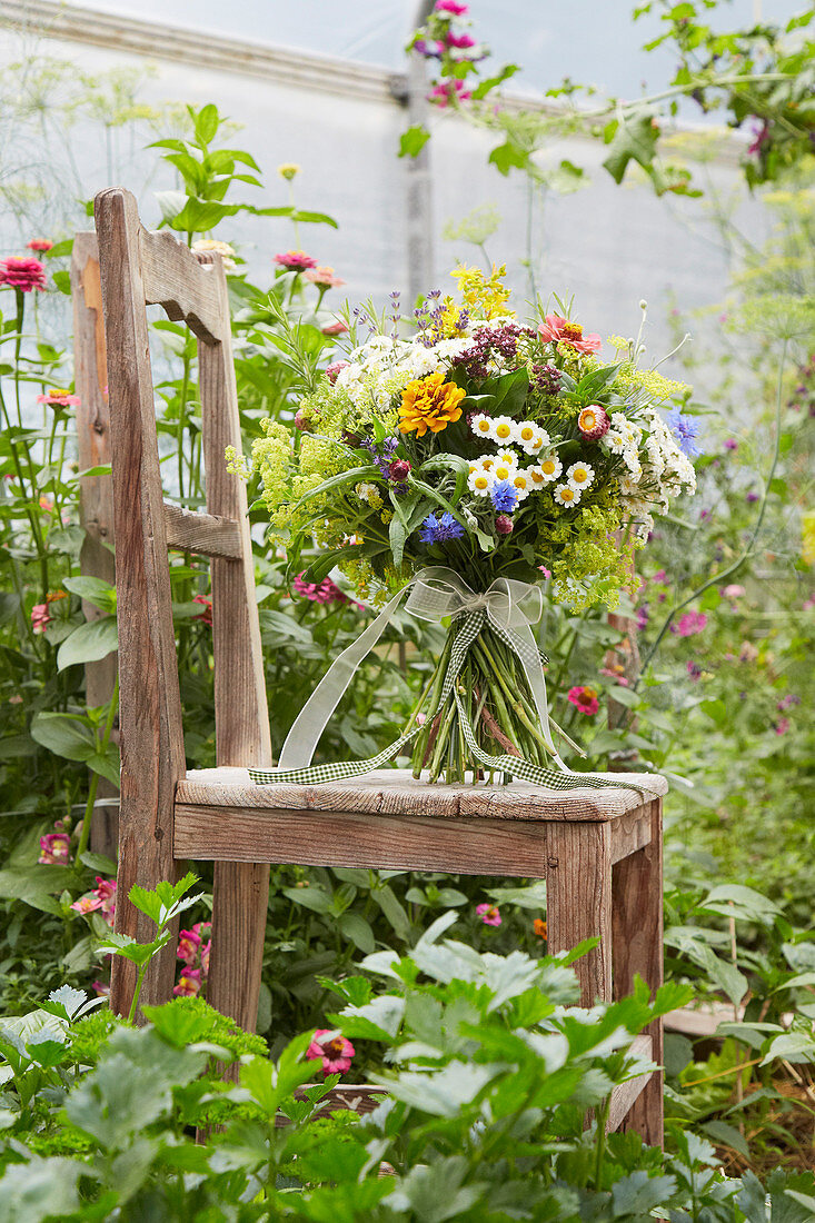 Sommerlicher Blumenstrauß steht auf einem Stuhl im Gewächshaus