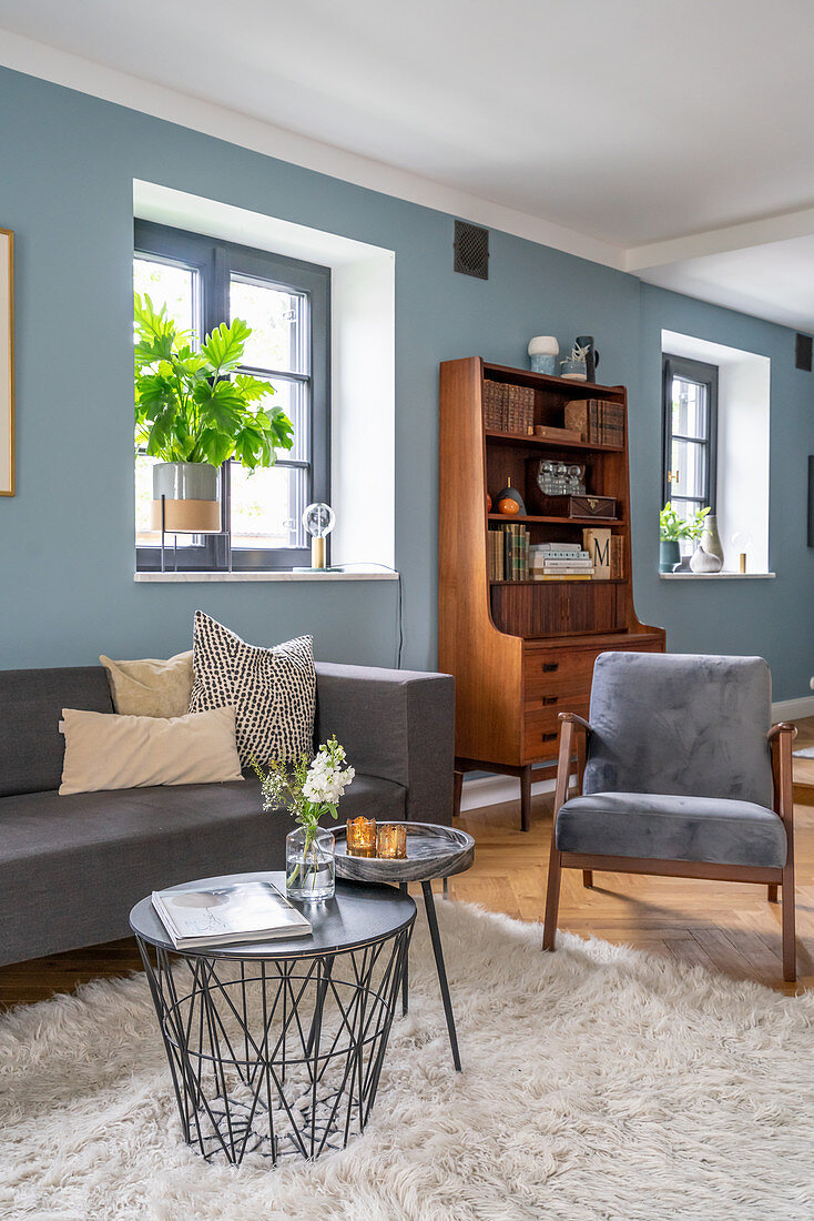 Graue Polstermöbel, Couchtisch und Retro Bücherschrank im Wohnzimmer mit blauer Wand
