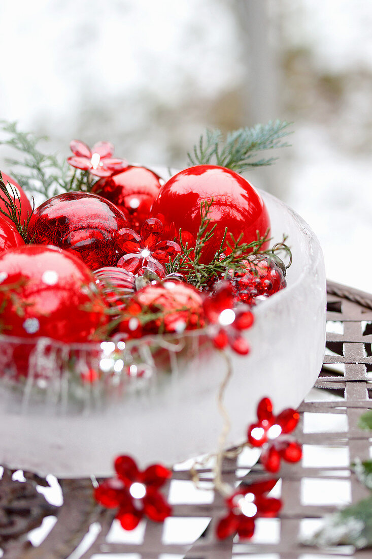 Schale aus Eis mit Lichterkette und roten Weihnachtsbaumkugeln