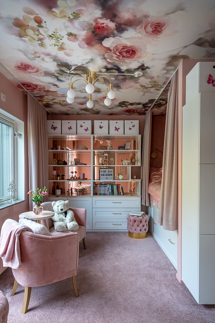 Girl's bedroom decorated in pink with floral wallpaper on ceiling, cubby bed and bookcase