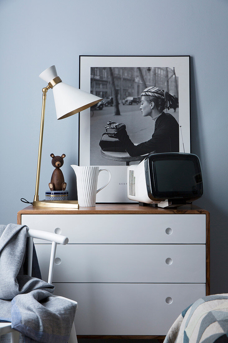 Black-and-white photo, TV and table lamp on top of chest of drawers